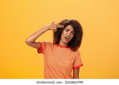I would rather kill myself. Displeased bored and dissatisfied attractive bothered girlfriend in striped t-shirt tilting head, grimacing from dislike putting finger gun to forehead, commiting suicide