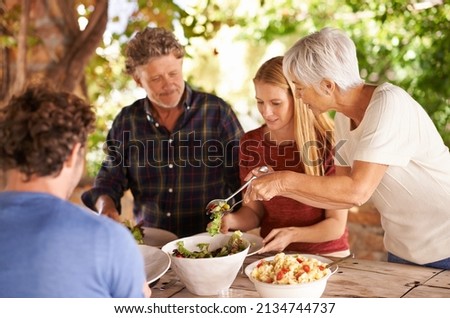 Would you like a little more. A view of a family preparing to eat lunch together outdoors.