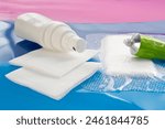 Wound management concept. Disinfection solution on two cotton gauze swabs and ointment tube on foam dressing for wounds and ulcers on turquoise and pink background