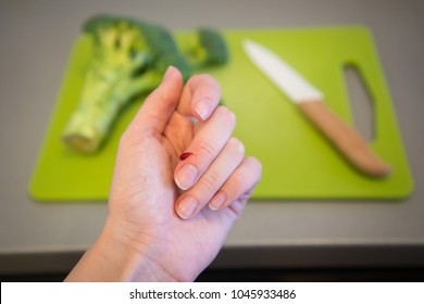Wounded finger with blood and knife on cutting board with broccoli