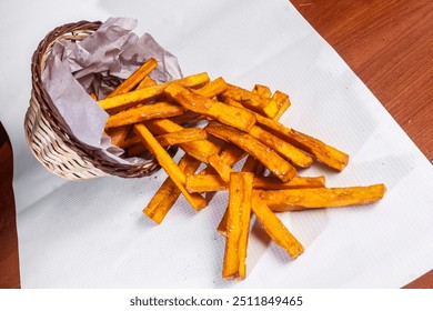 A woven checkerboard basket, overflowing with crispy sweet potato fries, scattered over a table, ready for a delicious snack or side dish. - Powered by Shutterstock