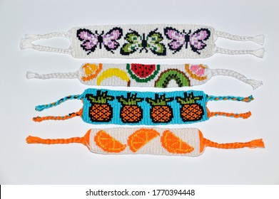 Woven friendship bracelets with alpha pattern fruit and butterflies handmade of thread on white background