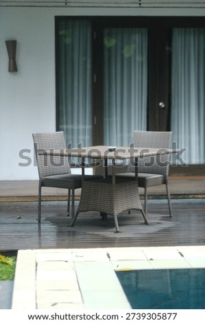 Woven table and two matching chairs placed on a veranda in front of a villa, creating a cozy outdoor seating area