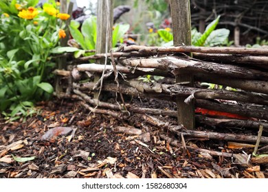 Woven Wattele Edge Of A Raised Garden With Center Wattle Basket For Compost In Keyhole Style.  Close Up Of Outer Wall With Calendula Flowers Outside And Winter Veg Inside.