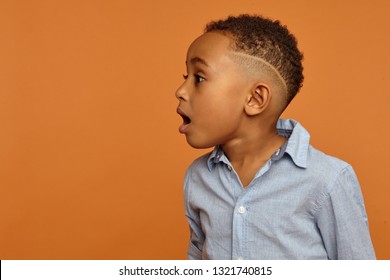 Wow. Amazed astonished handsome Afro American child with stylish hairdo posing isolated at blank copyspace studio wall, opening mouth widely, expressing great surprise and fascination, jaw dropped