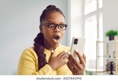 WOW. Beautiful woman looks at mobile phone with surprised open mouthed expression as she wins prize, earns money, sees unbelievable post on social media, watches shocking video, or finds special offer - Powered by Shutterstock