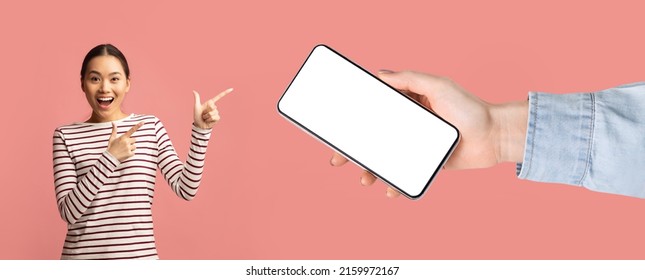 Wow, Check This Great Offer. Excited surprised Asian lady pointing fingers at big blank cell phone screen, huge hand holding device with white empty display on pink studio wall, banner panorama