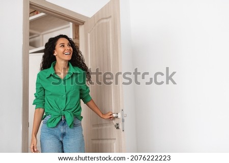 Wow. Cheerful lady walking in modern flat, entering new home, happy young female standing in doorway of apartment, holding doorknob handle looking at design interior, coming inside, free copy space
