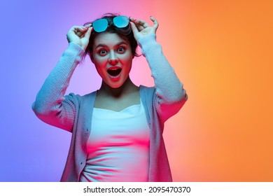 Wow emotions  Beautiful young girl waering sunglasses isolated gradient blue  orange color background in neon  Concept emotions  facial expression  youth  aspiration  Looks excited  surprised