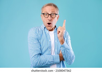 Wow, Eureka. Portrait Of Emotional Mature Man Having Great Idea, Finding Inspiration Or Solution To Problem. Excited Amazed Guy In Glasses With Open Mouth Pointing Finger Up On Blue Studio Background