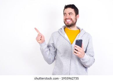 Wow!! Excited Young Caucasian Man Wearing Tracksuit Over White Background Showing Mobile Phone With Open Hand Gesture