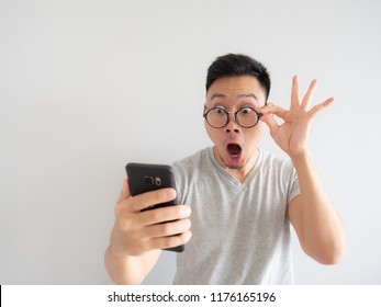 Wow face of Asian man shocked what he see in the smartphone on isolated grey background.