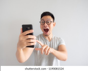 Wow Face Of Asian Man Shocked What He See In The Smartphone On Isolated Grey Background.