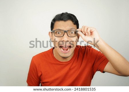 Wow face of Asian man wearing glasses in orange t-shirt shocked what he see in the smartphone on isolated background