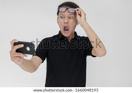 Wow face of Your Asian man shocked what he see in the smartphone on isolated grey background. Indonesia Man wear black shirt Isolated grey background.