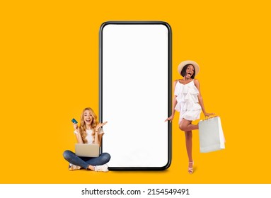 Wow, Fast Online Shopping Concept. Excited Black Woman In Summer Hat Dancing Near Big Giant Phone Screen, Smiling Lady Sitting On Floor Using Pc Holding Credit Card, Yellow Orange Studio Background