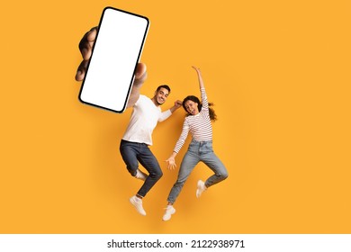 Wow, great news. Overjoyed couple showing huge smartphone with blank white screen, jumping and celebrating victory over orange studio background, mockup collage - Shutterstock ID 2122938971