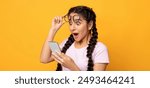 Wow, Great News. Portrait Of Excited Surprised Indian Woman Holding And Using Smartphone, Browsing Social Media. Emotional Young Lady Having Success, Taking Off Glasses, Yellow Studio Background