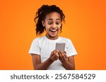 Wow, Great News. Portrait Of Excited Black Girl Celebrating Win, Holding And Using Smartphone Looking At Gadget Screen, Smiling Young Lady Having Success, Yellow Studio Background