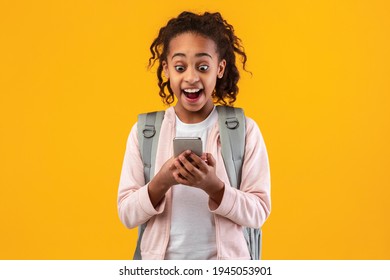 Wow, Great News. Portrait Of Surprised Excited Black Girl Using Smartphone And Reading Unexpected Sms Or News, Happy Smiling Teen With Open Mouth Holding Cellphone, Yellow Studio Background