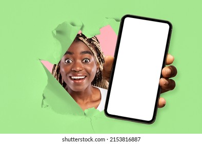 Wow, Great Offer. Excited Young Black Lady Holding Big Smartphone With White Blank Screen In Hand, Showing Close Up To Camera Through Torn Green Paper Hole. Gadget With Empty Free Copy Space, Banner