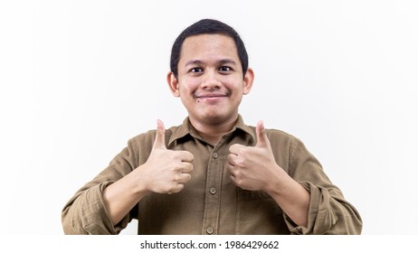 Wow and impressed face reaction of young Asian Malay man with two thumbs up and brown shirt on isolated white background.