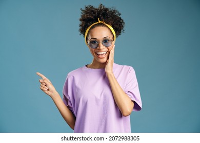 Wow Look At Advertise. Portrait Of Excited, Surprised Woman Pointing Side And Looking With Shocked Face, Showing Place For Commercial. Indoor Studio Shoot Isolated On Blue Background 