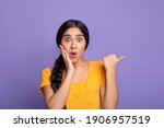 Wow, Look Here. Amazed young indian woman pointing at copy space over purple studio background. Excited surprised lady indicating free space, showing place for advert or promotional text