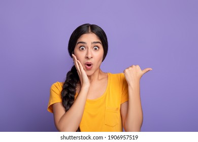 Wow, Look Here. Amazed young indian woman pointing at copy space over purple studio background. Excited surprised lady indicating free space, showing place for advert or promotional text - Shutterstock ID 1906957519