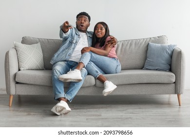 Wow, Omg. Portrait Of Emotional Excited African American Couple Watching TV Show Or Movie With Open Mouth, Hugging Sitting On Couch. Shocked Guy Holding Remote Control, Family Hearing Breaking News