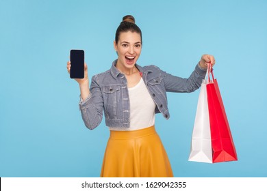 Wow, Online Store! Portrait Of Pleasantly Surprised Attractive Woman Expressing Excitement Amazement, Holding Packages And Cellphone, Advertising Of Mobile Shopping. Indoor Studio Shot Blue Background