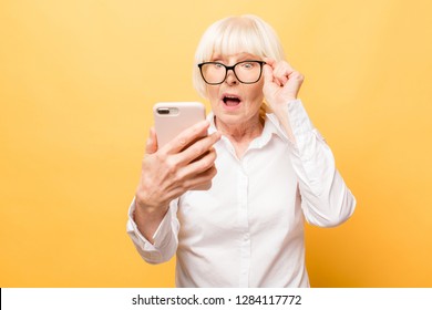 Wow! Phone conversation. Surprised aged woman using phone, isolated over yellow background. 