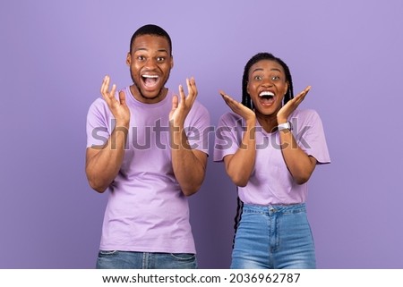 Wow. Portrait of overjoyed young black man and woman with open mouth gesturing in amazement looking at camera. Emotional surprised couple posing standing isolated over purple studio background wall