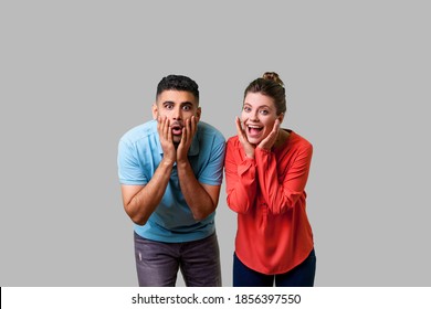 Wow! Portrait Of Shocked Attractive Young Couple In Casual Wear Standing Together, Holding Hands On Face With Surprised Amazed Expression, Open Mouth. Isolated On Gray Background, Indoor Studio Shot