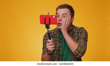 Wow Reaction. Impressed Man Blogger Taking Selfie On Mobile Phone Selfie Stick, Communicating Video Call Online With Subscribers. Young Teen Guy Boy 20s Isolated Alone On Yellow Studio Wall Background