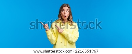 Wow something interesting. Intrigued and surprised alluring blond woman in yellow hoodie talking about last rumors, pointing and looking right with impressed expression, blue background.