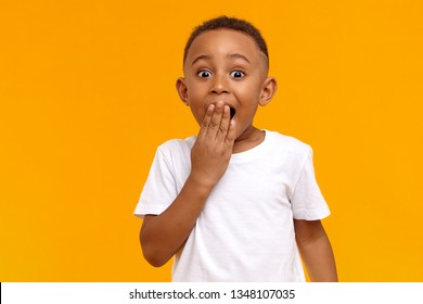 Wow. Studio shot of emotional adorable African American little boy raising eyebrows and covering open mouth with hand being surprised and shocked, showing true astonished reaction on unexpected news - Shutterstock ID 1348107035
