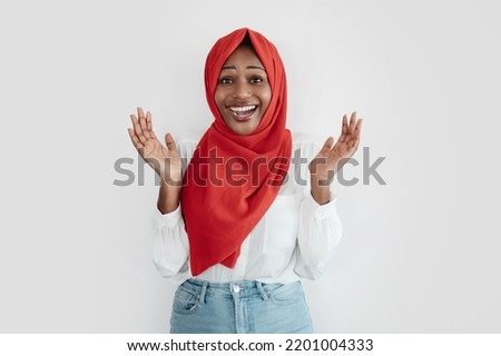 Wow. Surprised black muslim woman opened mouth in amazement and spreading hands, standing over light studio wall background, free space