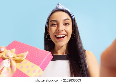 Wow, surprised emotions. Wide angle bottom view of young beautiful astonished girl holding gift box isolated on blue background. Concept of joy, holidays, inspiration, sales, ad. Happiness.