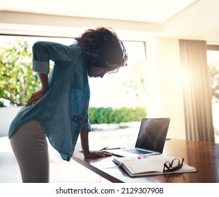 Wow, That Hurts A Lot. Shot Of A Young Woman Holding Her Back In Pain While Getting Up From Her Desk At Home.