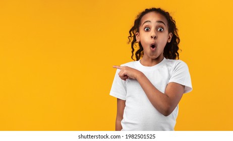 Wow, Unbelievable Offer Concept. Portrait Of Surprised African American Girl Pointing Finger Aside At Free Copy Blank Space For Text Standing On Yellow Orange Studio Wall. Look There, Panorama, Banner