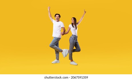 Wow, Yes. Portrait Of Overjoyed Young Couple Holding Hands, Excited Guy Raising Hand And Shaking Clenched Fist, Lady Showing Peace Sign Gesture. Casual Cool Couple Posing, Full Body Length, Free Space