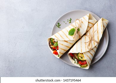 Wrap sandwich with grilled vegetables and feta cheese on a plate. Grey background. Copy space. Top view.