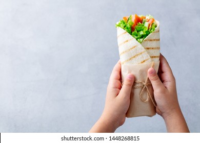 Wrap Sandwich In Kids Hands. Grey Stone Background. Top View. Copy Space.