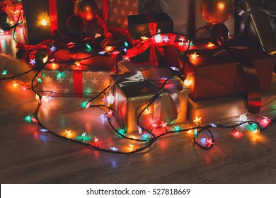 Wrapped present boxes decorated with red ribbon laying on the floor decorated with shining christmas led lights garland. Holiday evening decorations