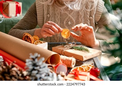 Wrapping christmas gifts. Blond woman wrapping presents in recycled card and decorated it with dried oranges and fir branches near the Christmas tree. Winter holiday celebration. - Powered by Shutterstock