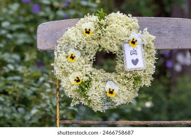 wreath of elder flowers and yellow viola flowers hanging on the garden chair - Powered by Shutterstock