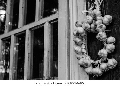 A wreath of garlic hangs on the wall of an old wooden house with small windows. Black and white. - Powered by Shutterstock