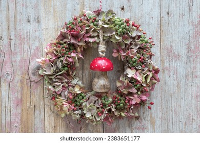wreath of hydrangea fklowers, rose hips and ivy berries hanging on the wooden wall