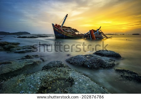 wrecked boat on a silent sea in sunset and golden twilight sky